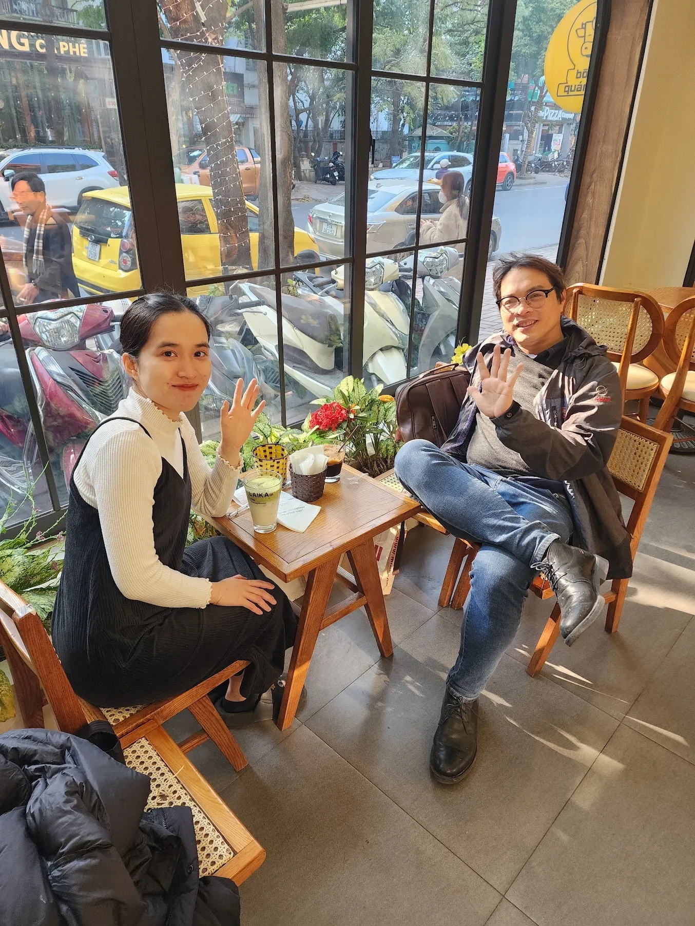 Hai người ngồi đối diện bên bàn gỗ trong quán cà phê, đồ uống đặt giữa bàn