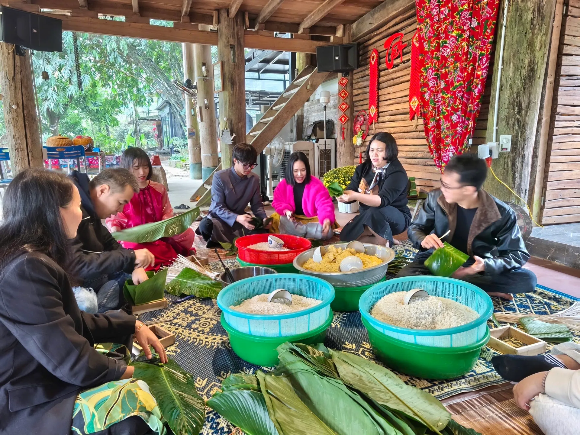 Cả nhóm ngồi trên chiếu gói bánh chưng ngày Tết trong gian nhà sàn ở Làng Hạnh Phúc 5M
